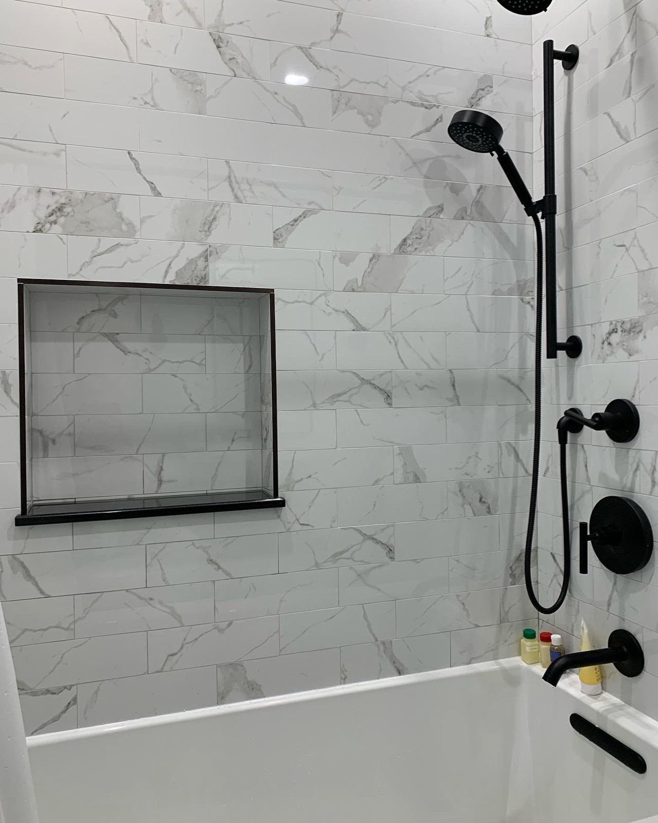 Marble-look tile tub surround with matte black fixtures and niche
