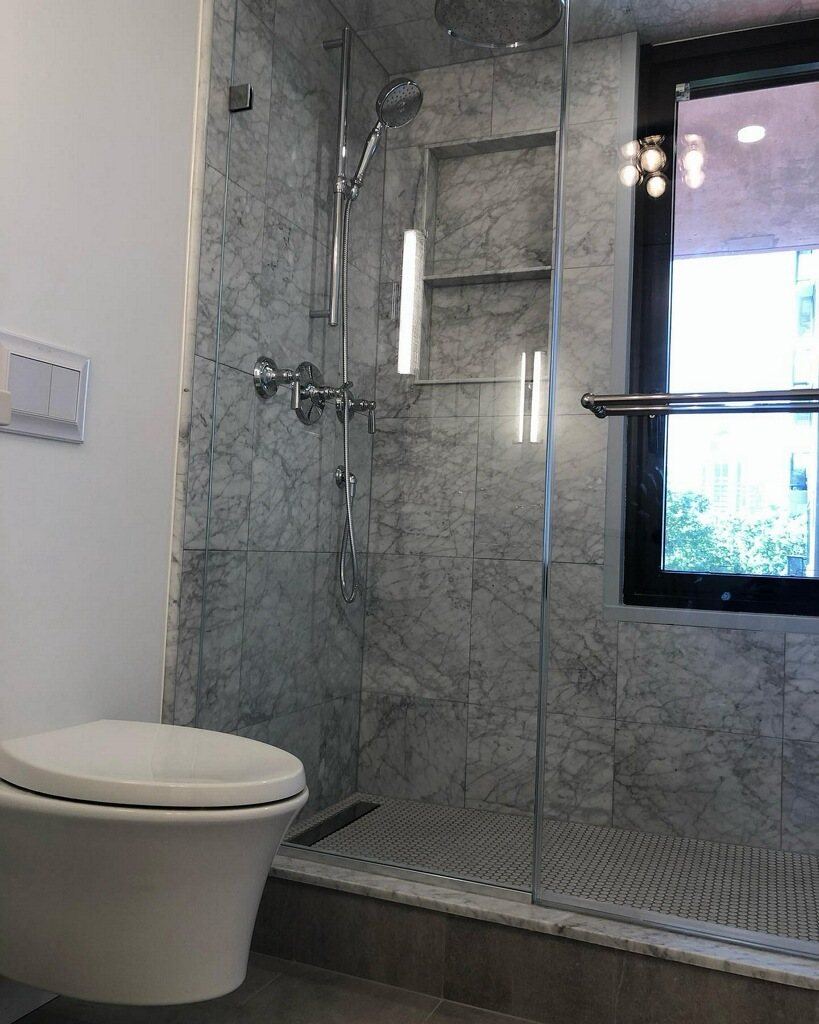 Carrara marble shower with linear drain and lit niche